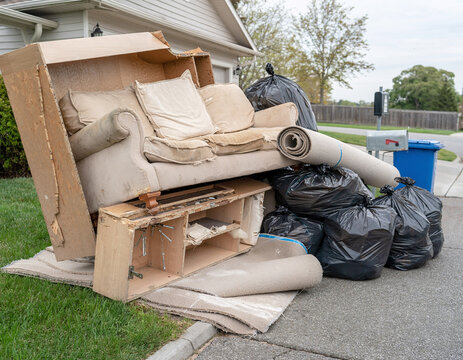 A bulky waste pile from a household renovation and cleanup project, consisting of old furniture and trash bags outdoors.