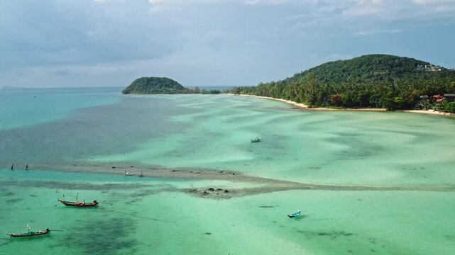 Koh Samui tropical island with clear turquoise shallow water, white sand beach, and several traditional longtail fishing boats floating near the lush green coastline, Aerial view panorama drone flight