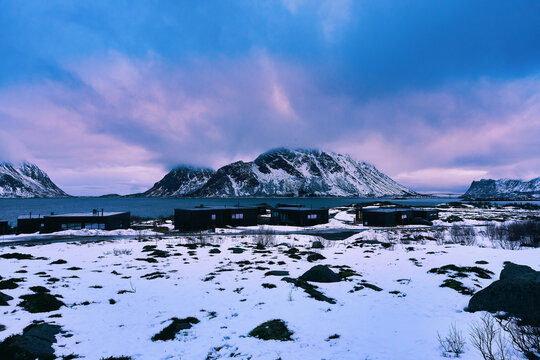 Majestic winter landscape of Lofoten islands in Norway at sunrise. Beautiful scenic view of snow-capped mountains under a vibrant golden hour sky with orange and purple colors in Arctic Scandinavia.