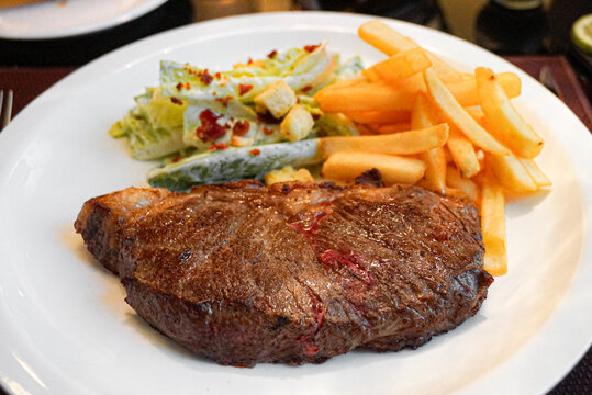 Grilled steak with fries and salad on a white plate