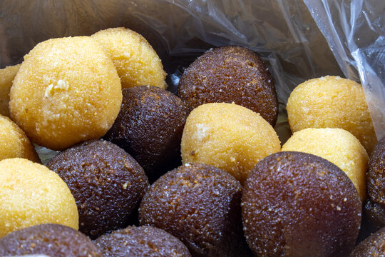 Assorted indian sweets, yellow besan laddu and dark brown gulab jamun balls, packed together in a clear plastic bag