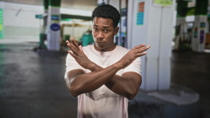 Man with arms crossed in an x gesture on a street at a gas station, wearing a light pink tshirt and looking stern  rejection resolve. © Krakenimages.com