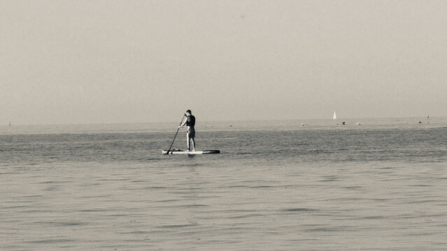 Person stand-up paddleboarding on calm water black and white