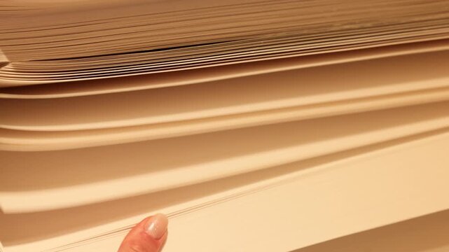 Finger flips through the thick pages of a paper stack