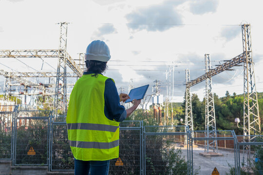 Engineer working on electrical substation infrastructure, holding a digital tablet for maintenance and monitoring power grid energy distribution processes