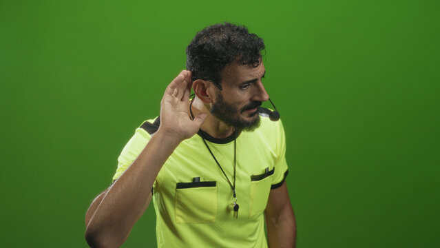 Man referee in yellow shirt pointing with hand, wearing whistle and headset in studio; authority discipline focus.