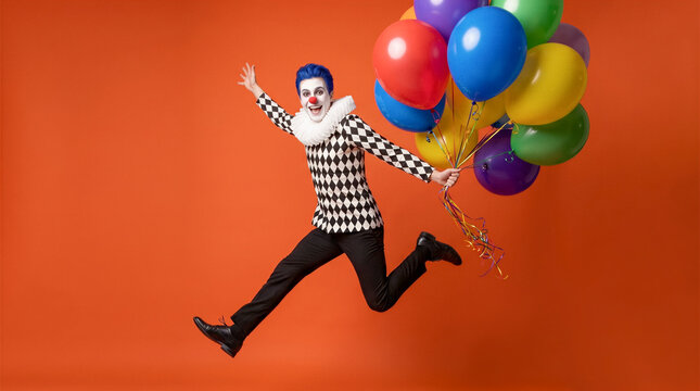 Clown jumping with colorful balloons against orange background. Entertainment, celebration, children s party, performance.