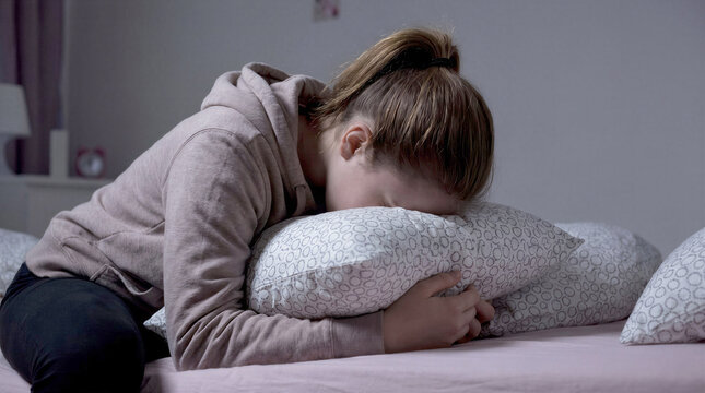 Sad teenage girl crying and burying her face in a pillow, mental health concept