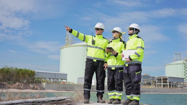 lng engineers pointing and discussing plant infrastructure outdoors, oil and gas project team examining terminal facility with laptop and tablet, industrial engineers planning at energy plant