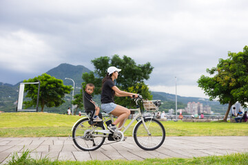 Fototapeta premium Mother riding bicycle with child near park