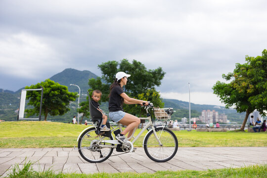 Mother riding bicycle with child near park