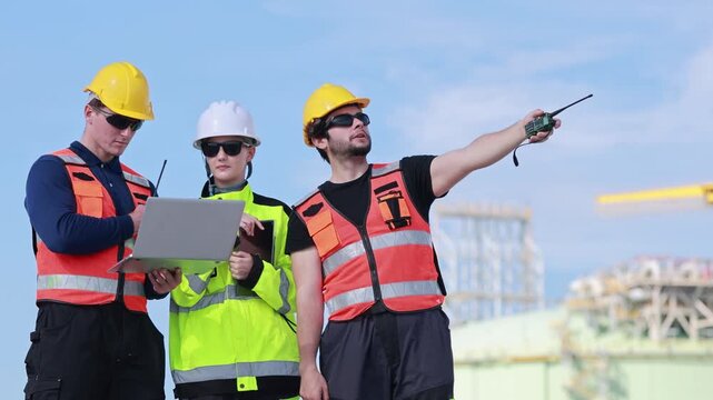 Lng engineers and technicians working with laptop and walkie talkie at plant, Oil and gas plant workers checking project details at energy facility