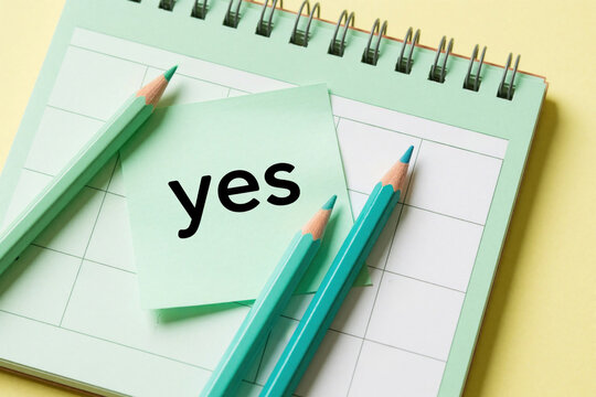 Close up view of calendar with yes word on sticky note. Green pencils lie on planner pages. Concept of positive decision, goal planning, commitment to new schedule. Minimalist stationery for business