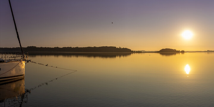 Serene morning sunrise over calm lake water with sailboat hull