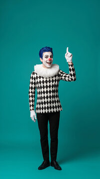 Clown pointing upward with one finger while looking at camera. Performance, entertainment, circus, celebration.