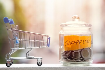 Miniature shopping cart next to a glass savings jar filled with coins for shopping budget shopping currency © mrzn