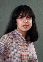 Obraz premium Portrait of a smiling young brunette woman in a plaid shirt against a green background.