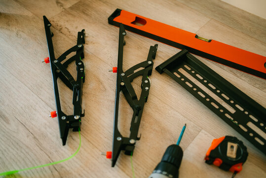 Tv wall mount components and tools laid out on wood floorbracket arms, horizontal support, drill, spirit level and measuring tape ready for diy installation and setup