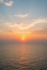 Obraz premium Sunset over ocean horizon. Sun rays pierce through clouds creating orange and yellow hues on calm sea water. Evening sky glows with soft light.