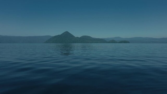 Low-angle view of the water surface with blue sky and Lake Toya's Nakajima Island in the distance