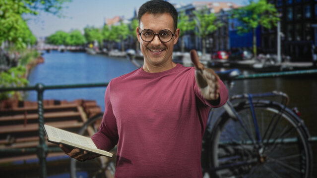 Man holding book and extending hand for handshake on a street by a canal with bicycle nearby; welcoming connection.