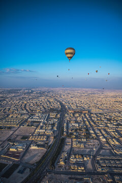 Hot air balloons fly over a sprawling city at sunrise
