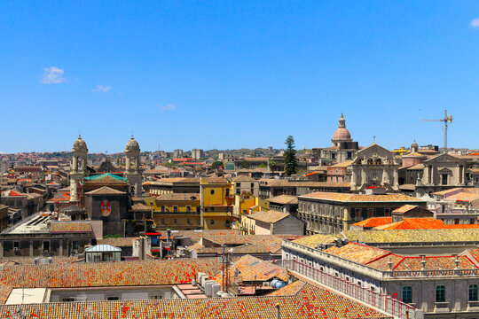 An aerial perspective showcases the dense urban landscape of a European coastal town, featuring classic tiled roofs and ornate buildings under a clear blue sky