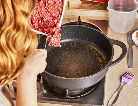 Teenager puts ground beef in frying pan for making spaghetti bolognese according to recipe from the Internet.