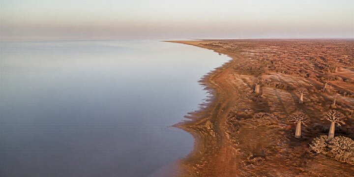 Aerial view of a tranquil lake beside an arid rocky shoreline. Natural landscape banner with expansive copy space for travel, environment, and nature concept design.
