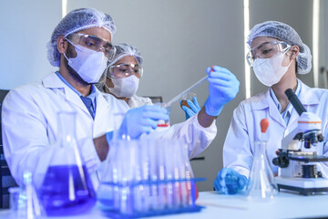 Scientists in lab coats and masks examine samples with a microscope and test tubes in a modern...