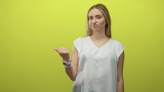 Woman with blonde hair in white blouse pointing left thumb to side in studio against lime green wall while grimacing and pursing lips; sarcasm dismissal.