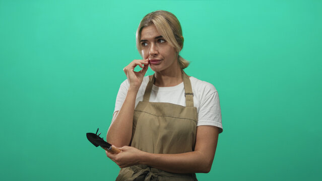 Woman gardener holding a hand trowel, gestures with hand and flicks fingers in studio; thoughtful reflection.
