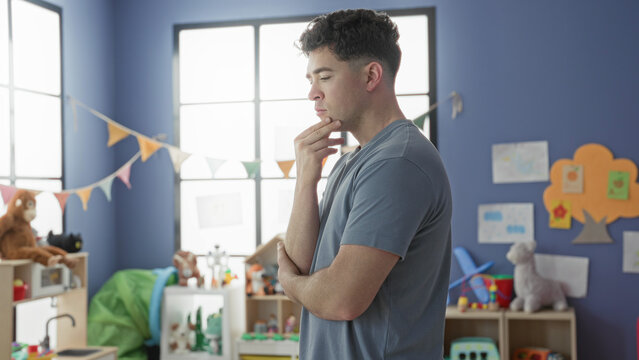 Man touching chin in a classroom building, surrounded by toys and bunting; thoughtful contemplation focus.