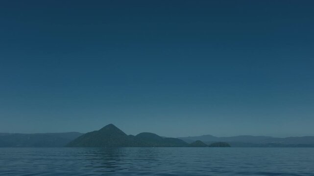 Low-angle view of the water surface with blue sky and Lake Toya's Nakajima Island in the distance