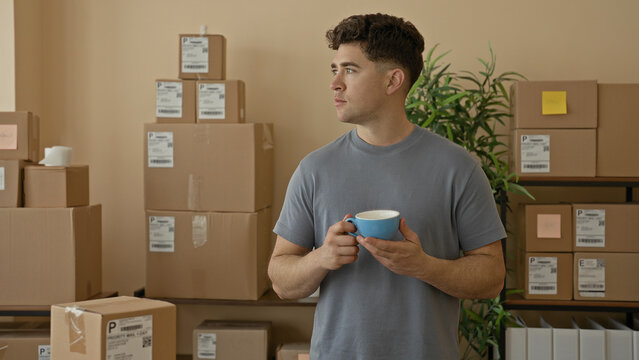 Man holding blue mug with both hands among stacked shipping boxes and labels in a building workspace; small business pride.