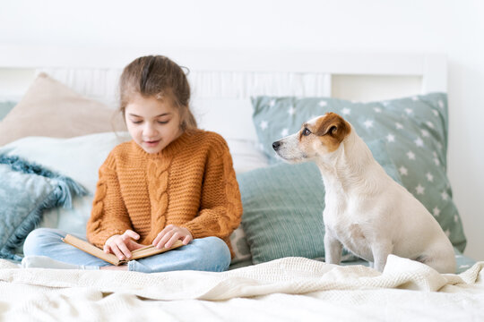 Caucasian child reads a book aloud to her dog sitting beside her, for content about speech development, literacy, reading practice and animal assisted therapy.