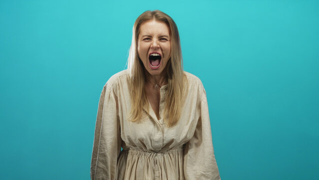 Woman with mouth open screaming, teeth and hands visible, expressive face against turquoise studio backdrop; anger release.