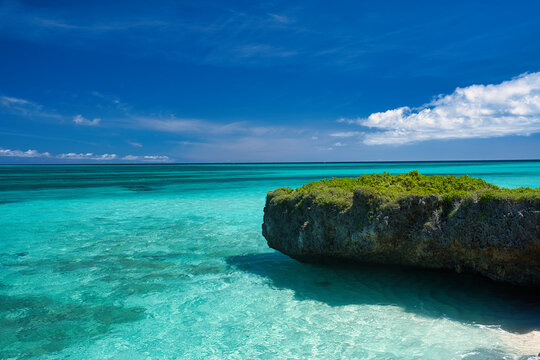 Undercut coral limestone rock and gradient of emerald green shallow sea under a blue summer sky, Miyakojima Island, Okinawa, Japan