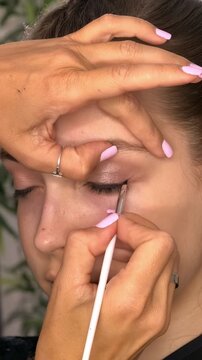 Beauty influencer draws eyeliner on a teenage girl's eye in close up, professional makeup, cosmetic styling, precise beauty application.