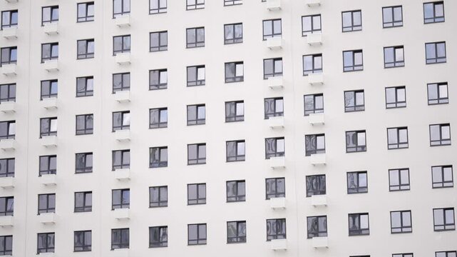 Modern white building exterior with grid pattern of windows wall-mounted air conditioners. Minimalist architectural detail under bright daylight. Neutral tones clean lines