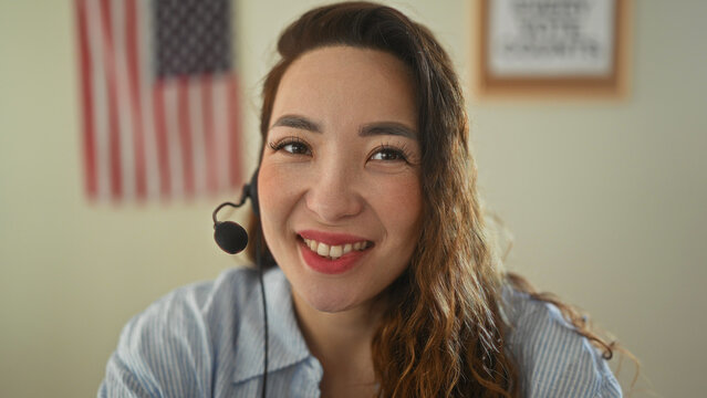 Woman with headset holding microphone and smiling, american flag visible on wall in campaign building; voter outreach pride.