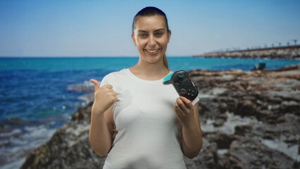 Woman holding gamepad and giving thumbs up in studio with seaside backdrop and smiling  happiness fun gaming. © Krakenimages.com
