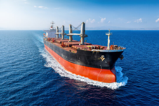 Close-up front view of a universal bulk carrier cargo ship traveling with high speed over blue ocean