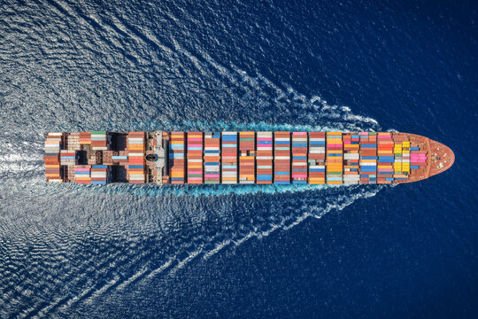 High aerial overhead view of a industrial super container cargo vessel sailing over the ocean with speed