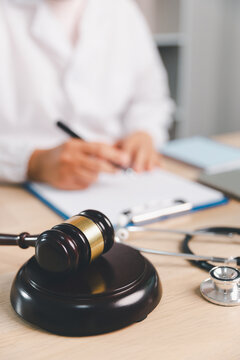 Healthcare law concept with gavel, stethoscope, clipboard and medical professional writing at office desk, representing malpractice, ethics, compliance, liability and legal medicine.