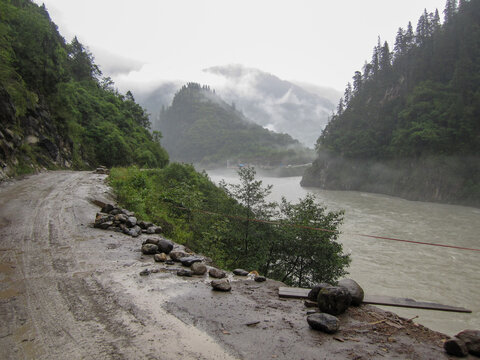 Misty mountain road by a river with lush greenery on both sides