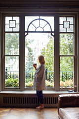 Fototapeta premium Thinking, relax or woman at window with coffee, morning reflection or calm moment on weekend break. Chill, back and person in house with mug, peaceful perspective and mindfulness at start of day.
