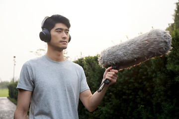 Young man with headphones holding boom microphone outdoors © HaXuanDieu