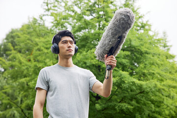 Man with headphones holding boom microphone in park © HaXuanDieu