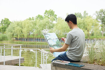 Young man painting outdoors by a lakeside in a park © HaXuanDieu